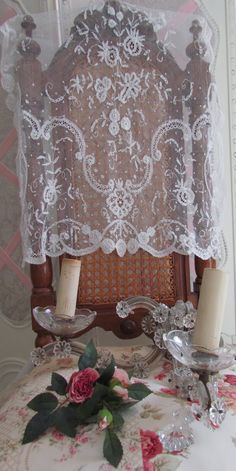 two candles are sitting on a table covered with white lace and pink roses, next to a candle holder