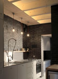 a kitchen with brick walls and white cabinets, lights on the ceiling above the sink