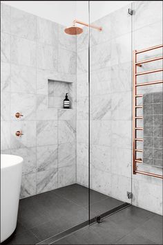 a white bathtub sitting next to a shower in a bathroom with marble walls and floors