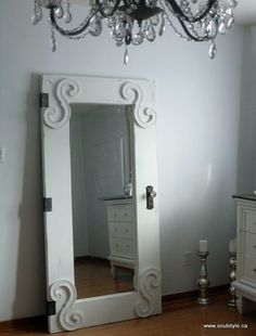 a white dresser with a mirror and a chandelier hanging from it's ceiling