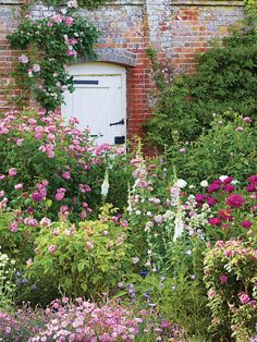 an old brick building surrounded by flowers and greenery with a white door in the center