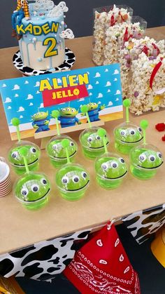 a table topped with lots of green cups filled with cake next to a sign that says alien hello