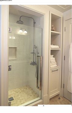 a walk in shower sitting inside of a bathroom next to a white robe hanging on the wall