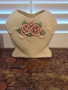 a heart shaped vase sitting on top of a wooden table next to some penny coins