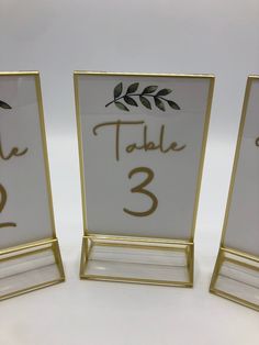 three gold and white place cards with leaves on them, one is for the table