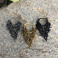 three pairs of black and gold earrings sitting on top of a rock next to flowers