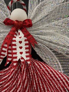 a red and white christmas angel decoration with hearts on it's chest, standing in front of a door