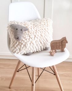 a sheep pillow sitting on top of a white chair next to a wooden toy animal