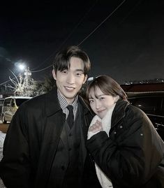 a man and woman standing next to each other in front of a car at night