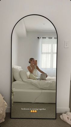 a woman sitting on top of a white bed in front of a large black mirror