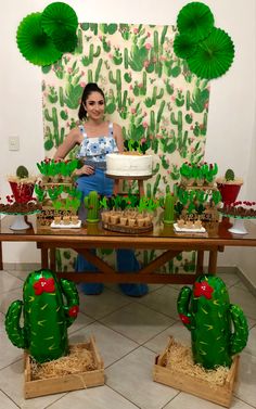 a woman standing in front of a table with cactus decorations and desserts on it