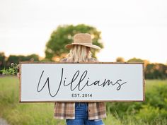 a woman holding a sign that says williams est 2014 in front of some grass and trees