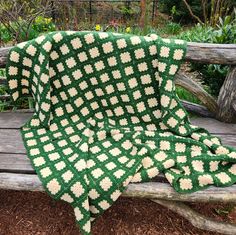 a green and white crocheted blanket sitting on top of a wooden park bench