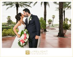 a bride and groom kissing in front of palm trees at their wedding reception, photographed by limelight photography