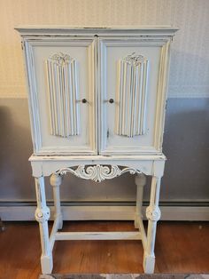 an old white armoire sitting on top of a hard wood floor next to a wall