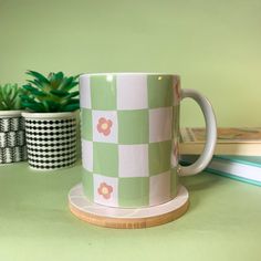 a green and white checkered coffee cup sitting on top of a table next to two books