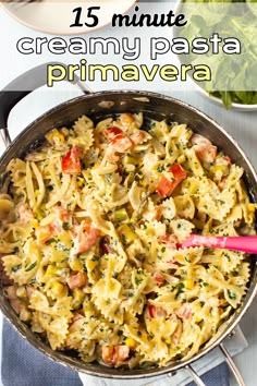 a pan filled with pasta and vegetables on top of a white table next to a pink spoon