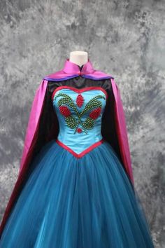 a dress made out of tulle and fabric with a cape on the top, in front of a gray background