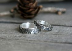 two silver rings sitting on top of a wooden table next to a pine cone and some cones