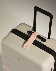 a white and black suitcase with a pink tag on it's handle, against a gray background