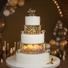 a three tiered wedding cake with lights on top and flowers in the middle, sitting on a table