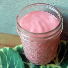 a glass jar filled with pink liquid sitting on top of a green leafy cloth