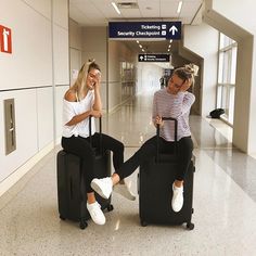 two women sitting on suitcases in an airport