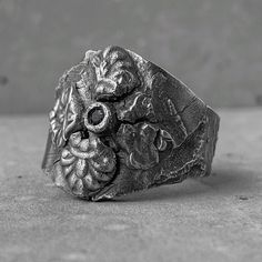 a silver ring with an ornate design on the front and center, sitting on a concrete surface