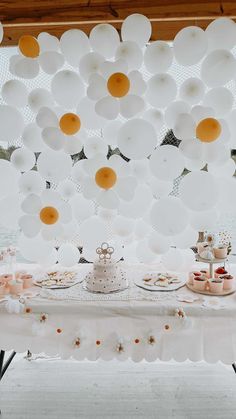 a table topped with lots of white balloons and plates filled with cake on top of it