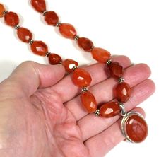 This is a handsome, handcrafted carnelian quartz and silver necklace with an oval pendant.  Each large carnelian bead was hand faceted.  Small spacer beads are silver rondels. The necklace was strung on beading wire for strength.     The carnelian stone beads feature natural inclusions, and range in their coloration.  Each bead is unique in its color, shape and facets.  There are no stamps on this necklace. DIMENSIONS Necklace length: 17 inches Number of hand-faceted carnelian beads: 20 Height o Silver Carnelian Beaded Necklace With Gemstone Beads, Beads Pendant, Carnelian Stone, Carnelian Beads, Beading Wire, Oval Pendant, Faceted Bead, Necklace Length, Jump Rings