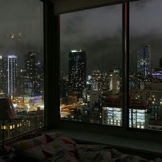 a view of the city at night from a bedroom in a skyscraper building, looking out on to the other side