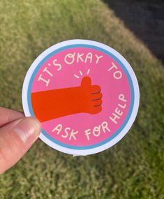 someone holding up a sticker that says it's okay to ask for help