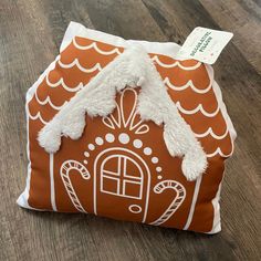 an orange and white pillow with a gingerbread house on it's front cover