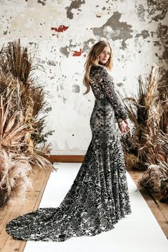 a woman in a long dress standing on a white rug with dried plants behind her