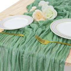 the table is set with plates and silverware, along with flowers on green chiffon