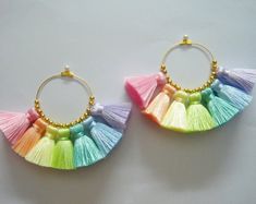 two pairs of colorful tasseled hoop earrings on white surface with gold beading