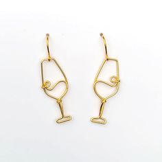 two pairs of gold - plated wire earrings on a white surface, one with a wine glass in the middle