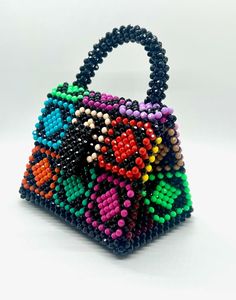 a handbag made out of beads on a white surface with a black handle and multicolored beading