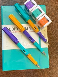 three pens sitting on top of a blue and yellow notebook next to two erasers