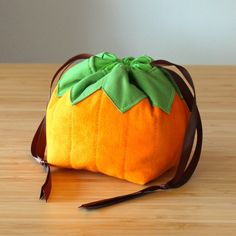 an orange purse with a green bow on it sitting on a wooden table next to a pair of scissors