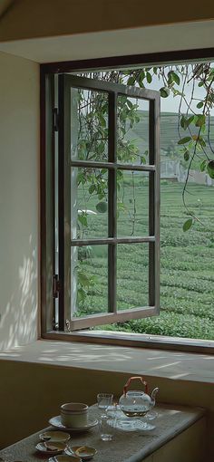 an open window overlooking a green field with tea cups and saucers on the table