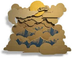 a paper cut out of clouds with a plane flying over the mountains in the background