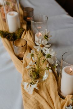 candles and flowers on a table with a cloth draped over it, along with other glass vases