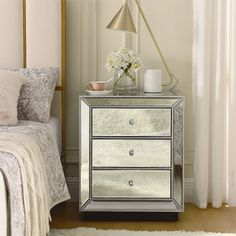 a bedroom with a white bed and a mirrored nightstand next to a window filled with curtains