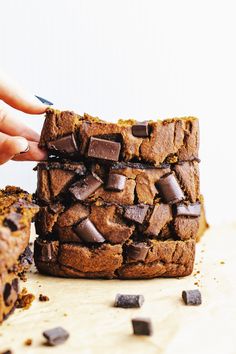 a person is grabbing a piece of chocolate chip cookie from a stack of brownies