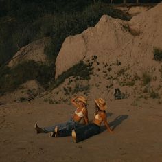 two women in bikinis laying on the beach with their heads down and one wearing a straw hat