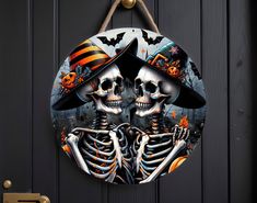 two skeletons dressed up in halloween costumes hanging on a black door with pumpkins and bats