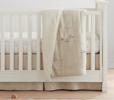 a white crib with two pillows and a blanket on the floor in front of it