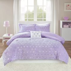 a purple bed with hearts on it in front of a window