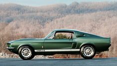 a green mustang muscle car parked in front of a mountain side with trees behind it